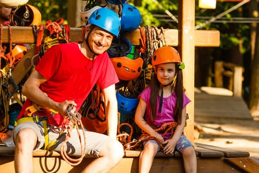 Adorable little girl enjoying her time in a rope playground structure at adventure park, her father supporting her, family weekend activities