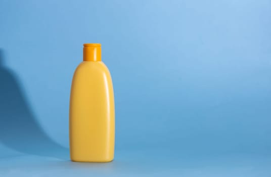 Yellow plastic cosmetic bottle on blue background. Kids hair shampoo, body lotion or sunscreen cream. Mock up, template