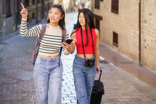 Two young Chinese women passing by guided by the GPS of their smartphone, through the streets of Granada, Spain. Concept of Asian people traveling in Europe.