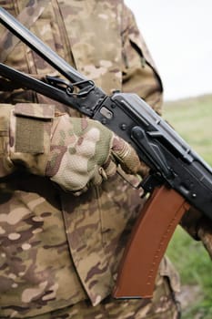 Military man holding AK-47 with tactical gloves closeup