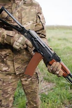 Military man holding AK-47 with tactical gloves closeup