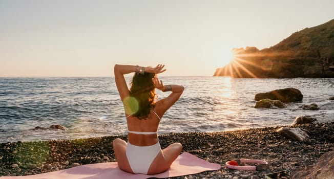 Young woman in swimsuit with long hair practicing stretching outdoors on yoga mat by the sea on a sunny day. Women's yoga fitness pilates routine. Healthy lifestyle, harmony and meditation concept.