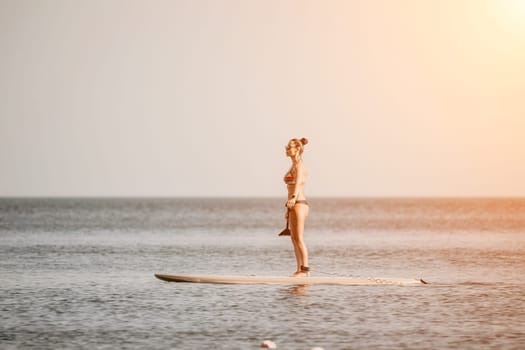 Sea woman sup. Silhouette of happy middle aged woman in rainbow bikini, surfing on SUP board, confident paddling through water surface. Idyllic sunset. Active lifestyle at sea or river