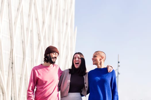 joyful trio of friends, one man and two women, laughing and hugging during a stroll, concept of friendship and urban lifestyle