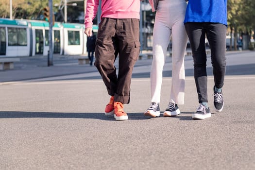 legs of three unrecognizable friends, one man and two women, walking on a sunny day, concept of friendship and urban lifestyle