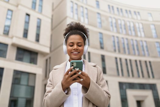 happy peaceful african girl tourist listening to podcast in wireless headphones while walking in the street.