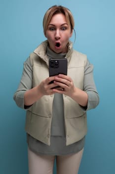 smiling surprised attractive blond girl showing blank smartphone screen with mockup for web page on blue background.
