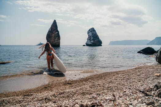 Close up shot of beautiful young caucasian woman with black hair and freckles looking at camera and smiling. Cute woman portrait in a pink bikini posing on a volcanic rock high above the sea