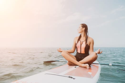 Woman sup yoga. Happy young sporty woman practising yoga pilates on paddle sup surfboard. Female stretching doing workout on sea water. Modern individual female outdoor summer sport activity