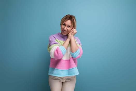 close-up of an embarrassed blond young woman in a striped sweater on a blue background with copy space.