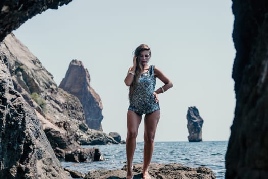 Woman travel sea. Young Happy woman in a long red dress posing on a beach near the sea on background of volcanic rocks, like in Iceland, sharing travel adventure journey