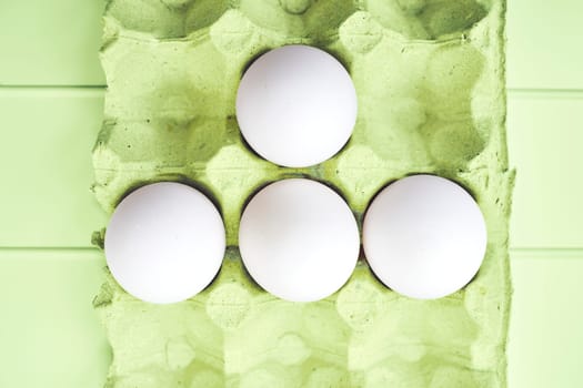an oval or round object laid by a female bird, reptile, fish, or invertebrate, usually containing a developing embryo. Four white eggs in a green carton on a green table.