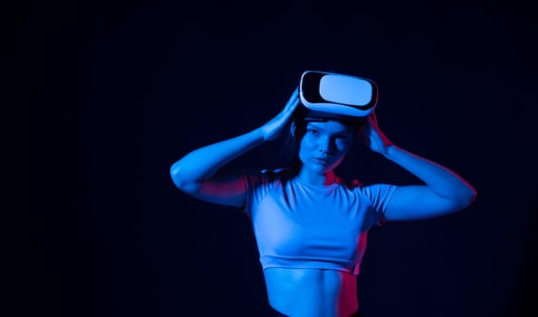 Portrait of young woman playing in VR-glasses in neon light on blue background. Concept modern gadgets and technologies. Future technology concept. Virtual reality gaming