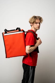 Smiling young courier with curly hair in red uniform with red thermo bag on white background. Food delivery service