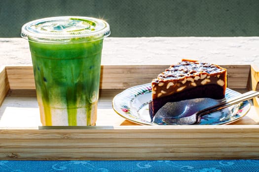 cake and Green tea Latte on outdoor wooden table in sunshine morning