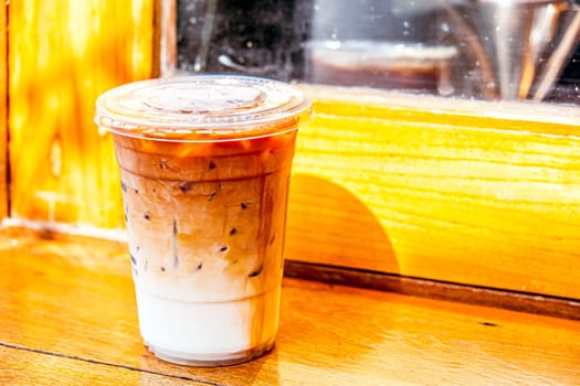 plastic glass of iced latte coffee with fesh milk on wood window
