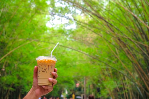 Woman hand holding the glass iced matcha latte green tea coffee on spring nature background