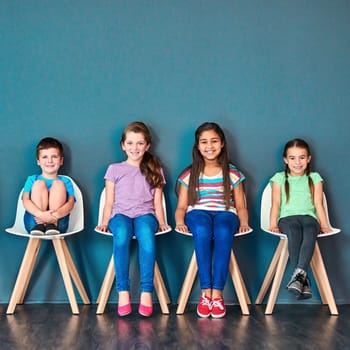 Its our turn now. Studio portrait of a diverse group of kids sitting on chairs in a line against a blue background