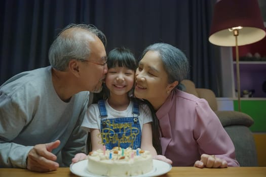 Happy Birthday. Asian family grandfather and grandmother kissed granddaughter feeling thankful while celebrating his birthday after giving wonderful cake, senior family party with child at home