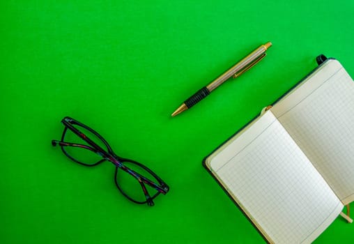 Desktop. Glasses, notebook and pen on a green background. Mockup diary. Business, freelancing, back to school.