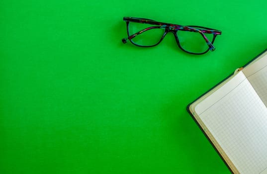Desktop. Notebook glasses on a green background, top view. Mockup diary. Business, freelancing, back to school.