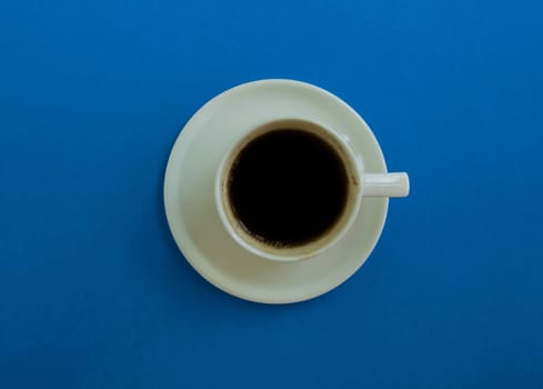 Cup of coffee on a blue background, top view. Cup of coffee with a saucer on a blue background, top view.