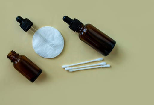 Flat lay bottles with a pipette for cosmetics and a cotton pad, and cotton buds on a beige background. Accessories for beauty salon, spa salon. Women's cosmetics, personal care.
