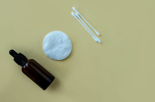 Flat lay bottle with a pipette for cosmetics, cotton buds and a cotton pad on a beige background. Accessories for beauty salon, spa salon. Women's cosmetics, personal care.