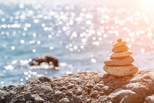 Tower of stones. Balanced pebble pyramid on the beach on a sunny day. Blue sea on the background. Selective focus, bokeh. Zen stones on the sea beach, meditation, spa, harmony, tranquility, balance concept.