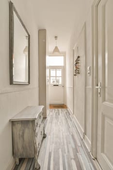 a hallway with wood flooring and white painted walls in the background is a mirror on the wall above it