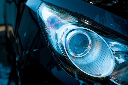 Car headlight with shallow depth of field.Black car in washing process