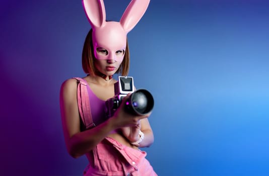 sexy girl in a pink bunny mask with a retro video camera in neon light on the background