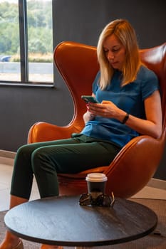 positive blonde businesswoman holding a mobile phone, happy to receive a message from her best friend or colleague, sitting in a cozy cafeteria at the table, High quality photo