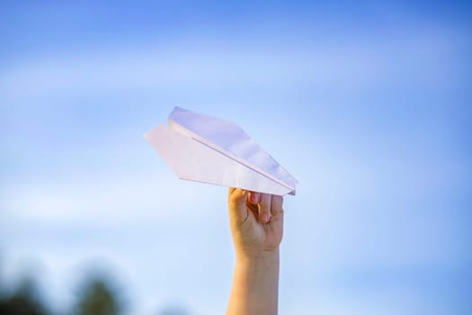 The boy's hand holds a white paper airplane against the sky. The topic of travel and air travel