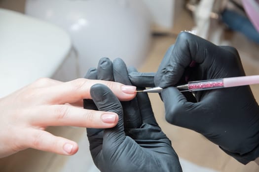 a master does a manicure to a client in a beauty salon and covers her nails with pink varnish, the master levels the edge of the varnish with a thin brush, High quality photo