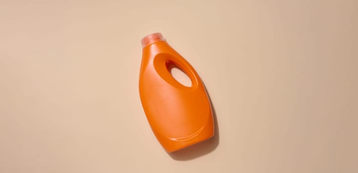 Orange plastic bottle for liquid detergents, for washing clothes on a beige background, top view