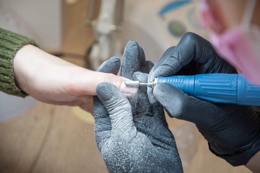 The manicurist grinds off the old coating from the client's nails with the help of a professional electric nail file. High quality photo