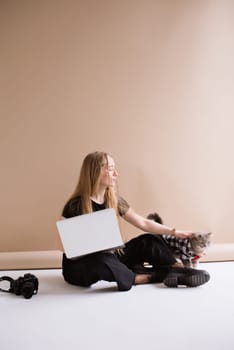 A business woman freelancer in a black is working, typing on a laptop apple and sitting on a white floor. blonde assistant in video production with computer MacBook and camera with cat