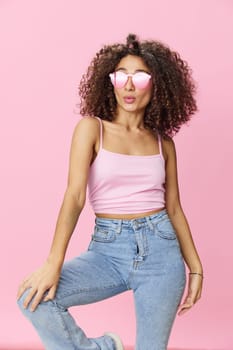 Happy woman afro curls hair dancing on a pink background in summer pink t-shirt jeans and glasses, summer vibe, copy space. High quality photo