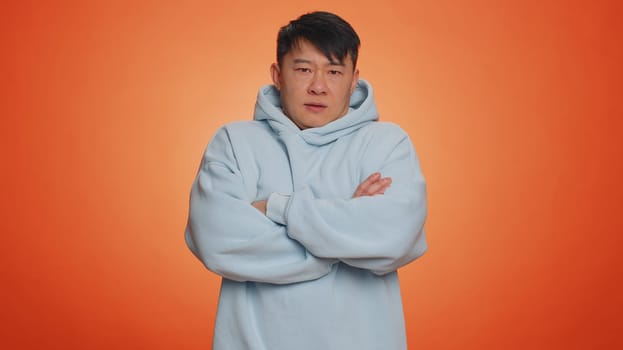 Offended sad nervous asian man having misunderstanding, frustrated after quarrel, fail, lose, ignores and does not want to communicate, talk. Guy isolated on orange studio background. People lifestyle
