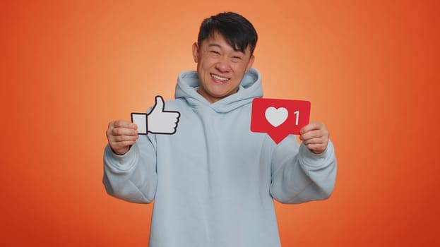 Like. Happy asian man raises inscription thumbs up banner thumbs up agrees with something, gives positive reply recommends advertisement likes good on social media. Guy on orange studio background