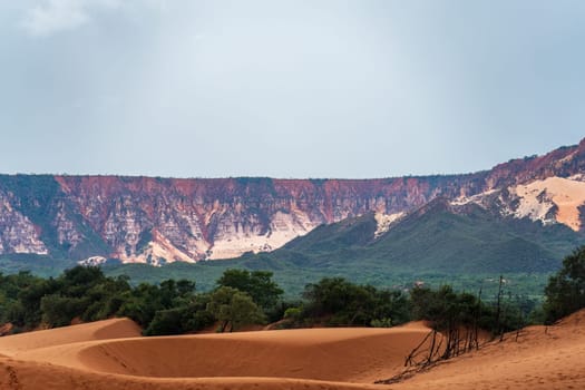 A breathtaking landscape with towering mountains, isolated sand dunes in the foreground, and lush greenery in between. The perfect representation of natural beauty and solitude.