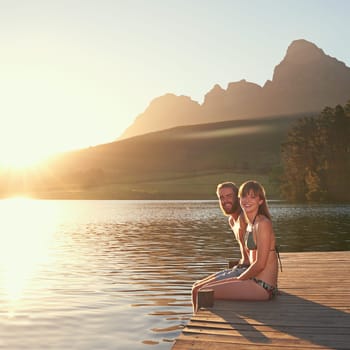 Enjoying a perfect day in paradise. an affectionate young couple in swimsuits sitting on a dock at sunset