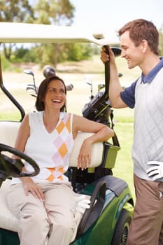 Love and laughter on the green. Smiling woman seated in a golf cart with her husband standing alongside her