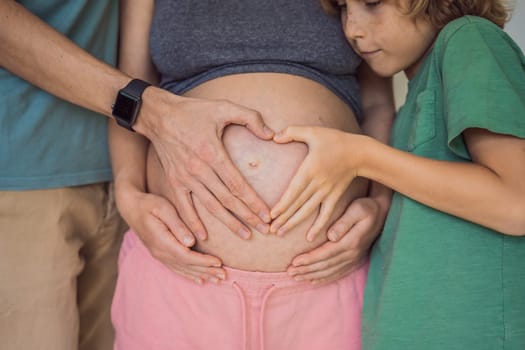 Pregnant Woman, father and first kid child holding hands in a heart shape on her baby bump. Pregnant Belly with fingers Heart symbol.
