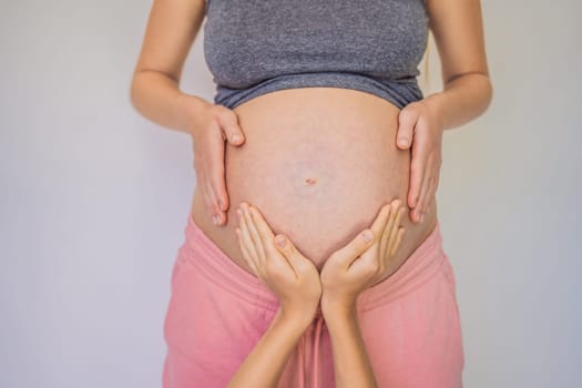 Young beautiful pregnant woman and eldest son. The cute boy put his hands on his mother's belly. Expecting a baby in the family concept. Preparing an older child for a younger one.