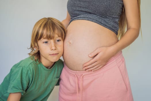 Young beautiful pregnant woman and eldest son. The cute boy leaned his ear against his mother's belly. Expecting a baby in the family concept. Preparing an older child for a younger one.