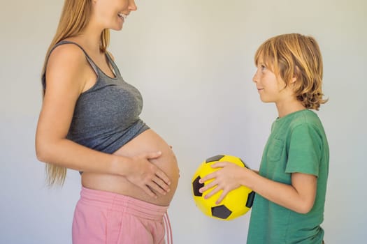 Amusing son. Pregnant beautiful woman amusing her little son while putting yellow ball under his green shirt.