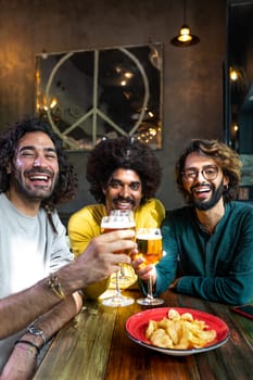 Happy young man showing to multiracial guy friends mobile phone while having drinks together in pub. Technology and leisure activity.