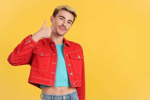 Happy gay man gesturing agreement raising a thumb up in studio with yellow background